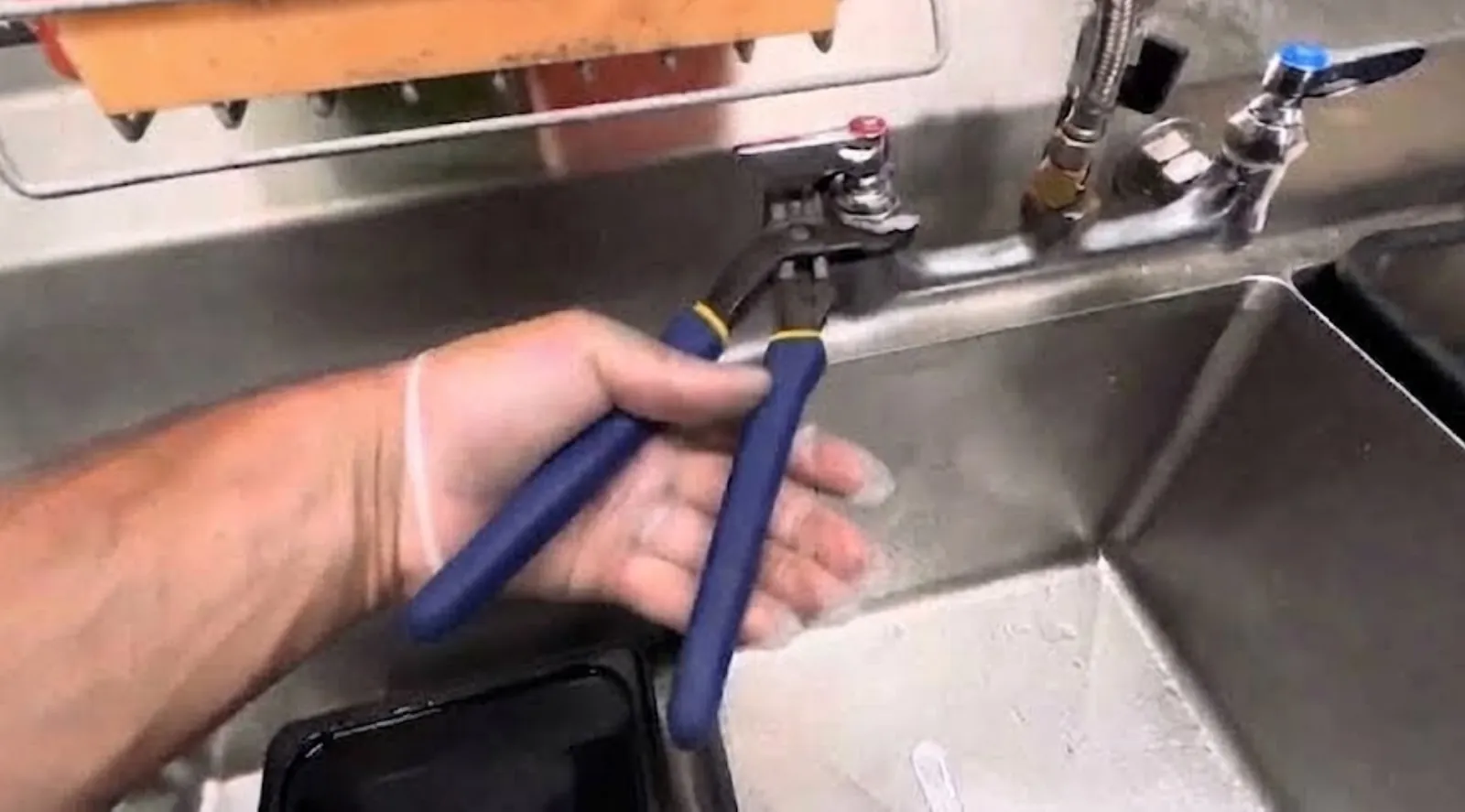 Plumber working on the faucet of a stainless steel commercial sink