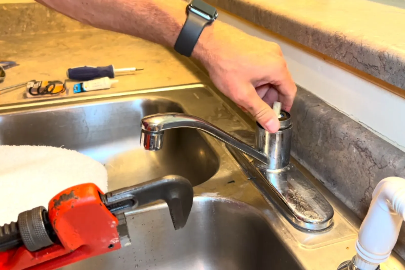 Plumber repairing a kitchen faucet with a pipe wrench nearby
